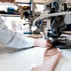A woman focused on sewing fabric at a sewing machine in a well-lit workspace.