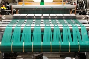 A machine producing green fabric, with threads being woven together in a textile manufacturing process