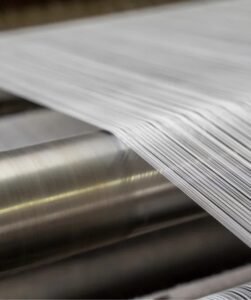Close-up of a metal roll with a long, unspooled strip of shiny metal extending from it.